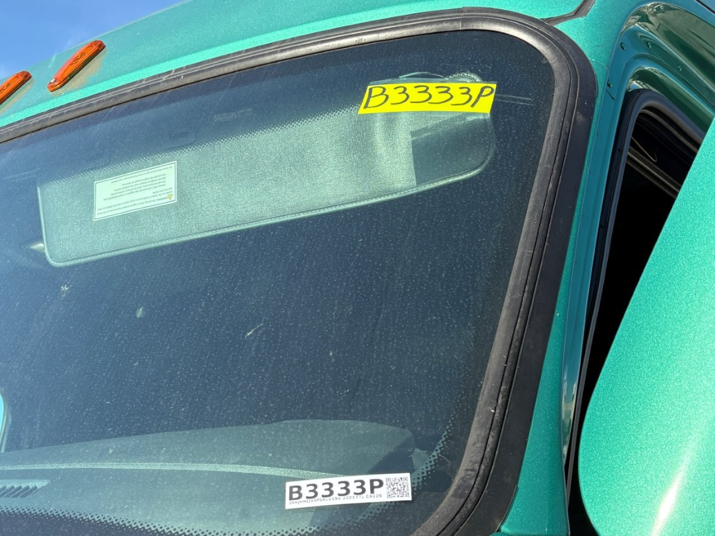 Truck cab window with B3333P sticker on windshield of a teal Freightliner Cascadia 126 sleeper in-service.