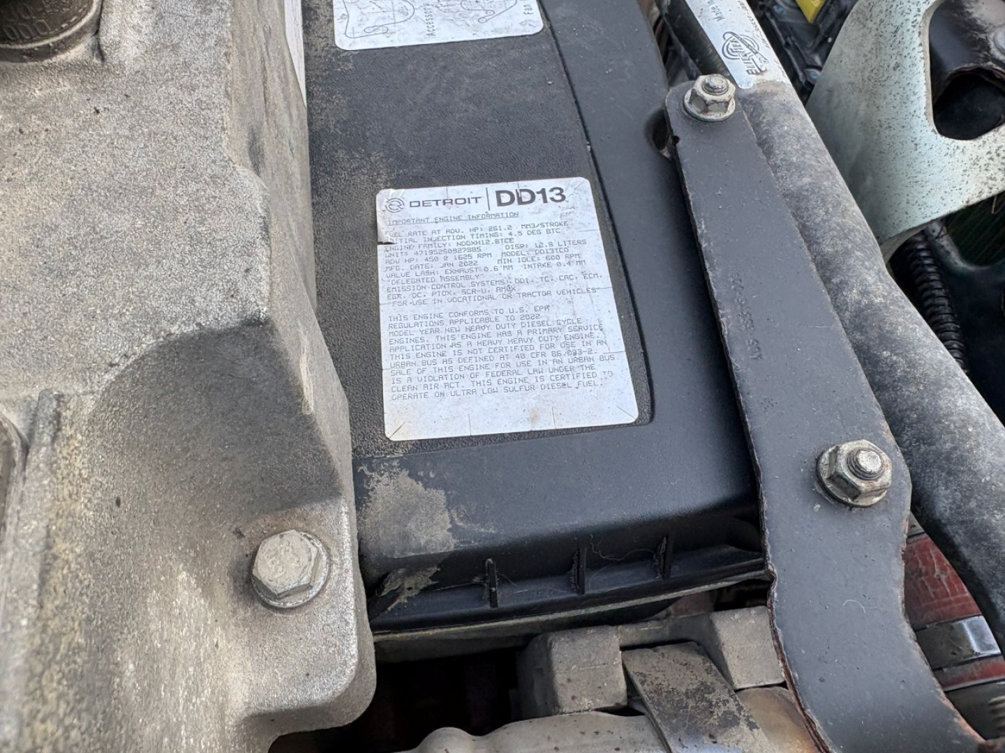 Engine bay showing a Ford Detroit DD13 label on the battery/air intake area with surrounding mounts and bolts.