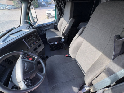 Cab interior of a 2023 Freightliner Cascadia 126 semi-truck showing driver seat, passenger seat, steering wheel, and dashboard with controls.