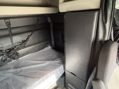 Freightliner Cascadia 126 sleeper cab interior showing storage cabinet and tarp-covered bed area, seat in foreground, gray upholstery.