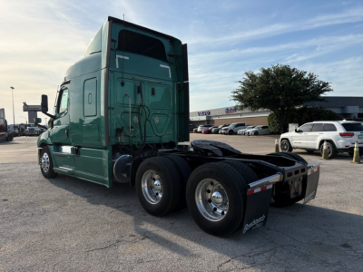 Freightliner Cascadia 126 tractor in a parking lot, rear view showing dual rear axles and fifth wheel with green cab.