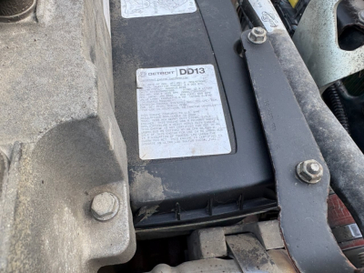 Engine bay showing a Ford Detroit DD13 label on the battery/air intake area with surrounding mounts and bolts.