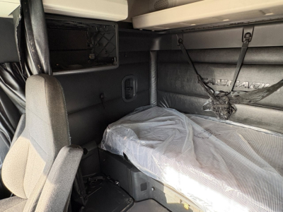 Interior of a Freightliner Cascadia sleeper cab showing bunk area with plastic-covered mattress, sidewall panels, and overhead cabinetry.