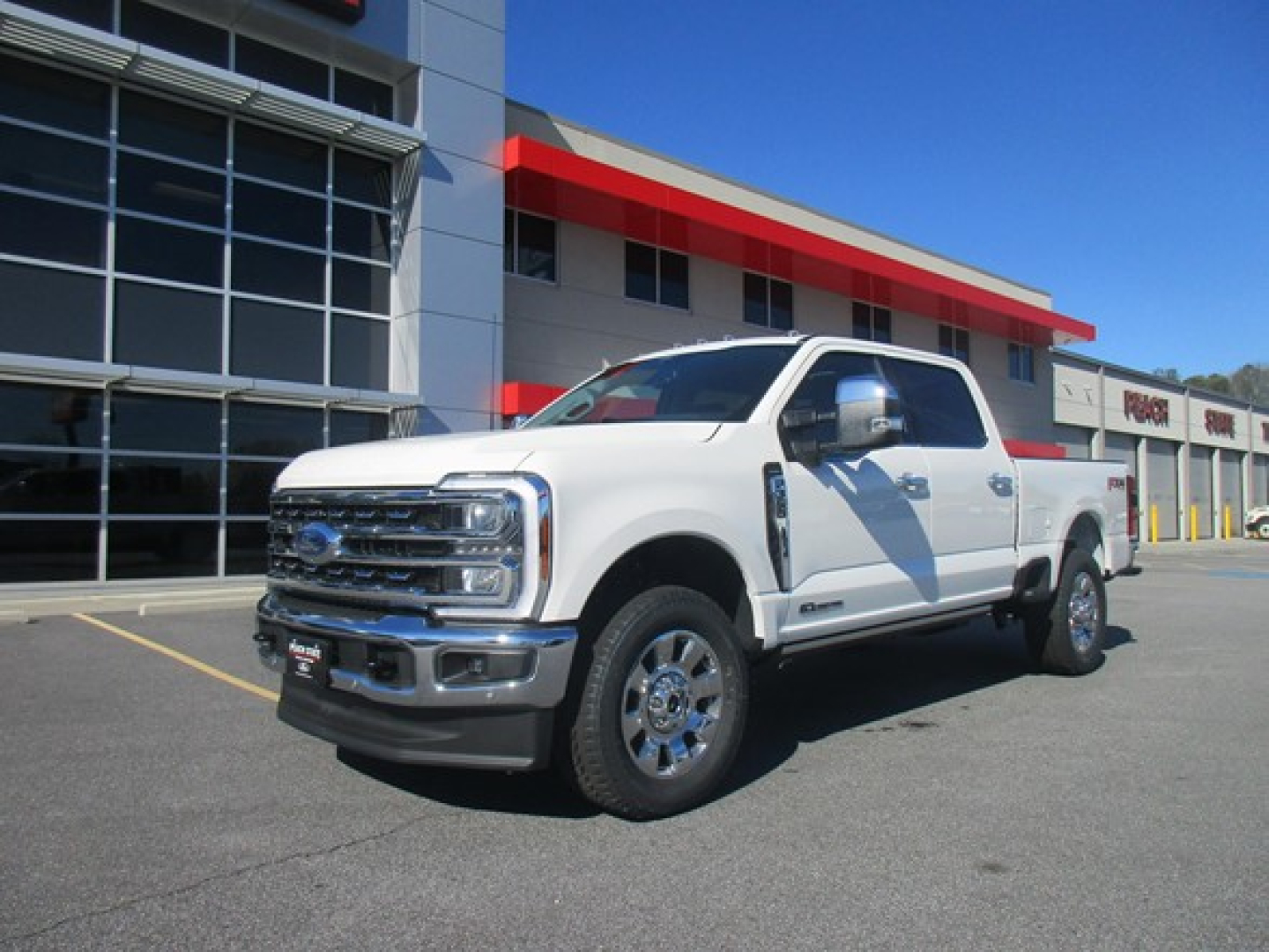 2026 Ford F350 white pickup truck in dealership lot with building and glass showroom in background.