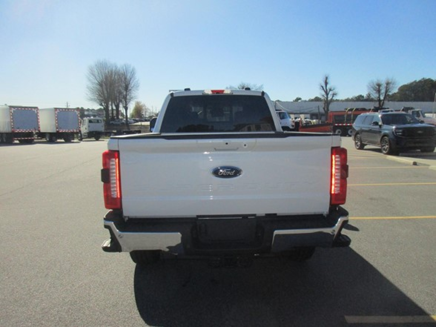 Ford truck rear view showing tailgate with Ford emblem and taillights; parking lot with other vehicles in background.
