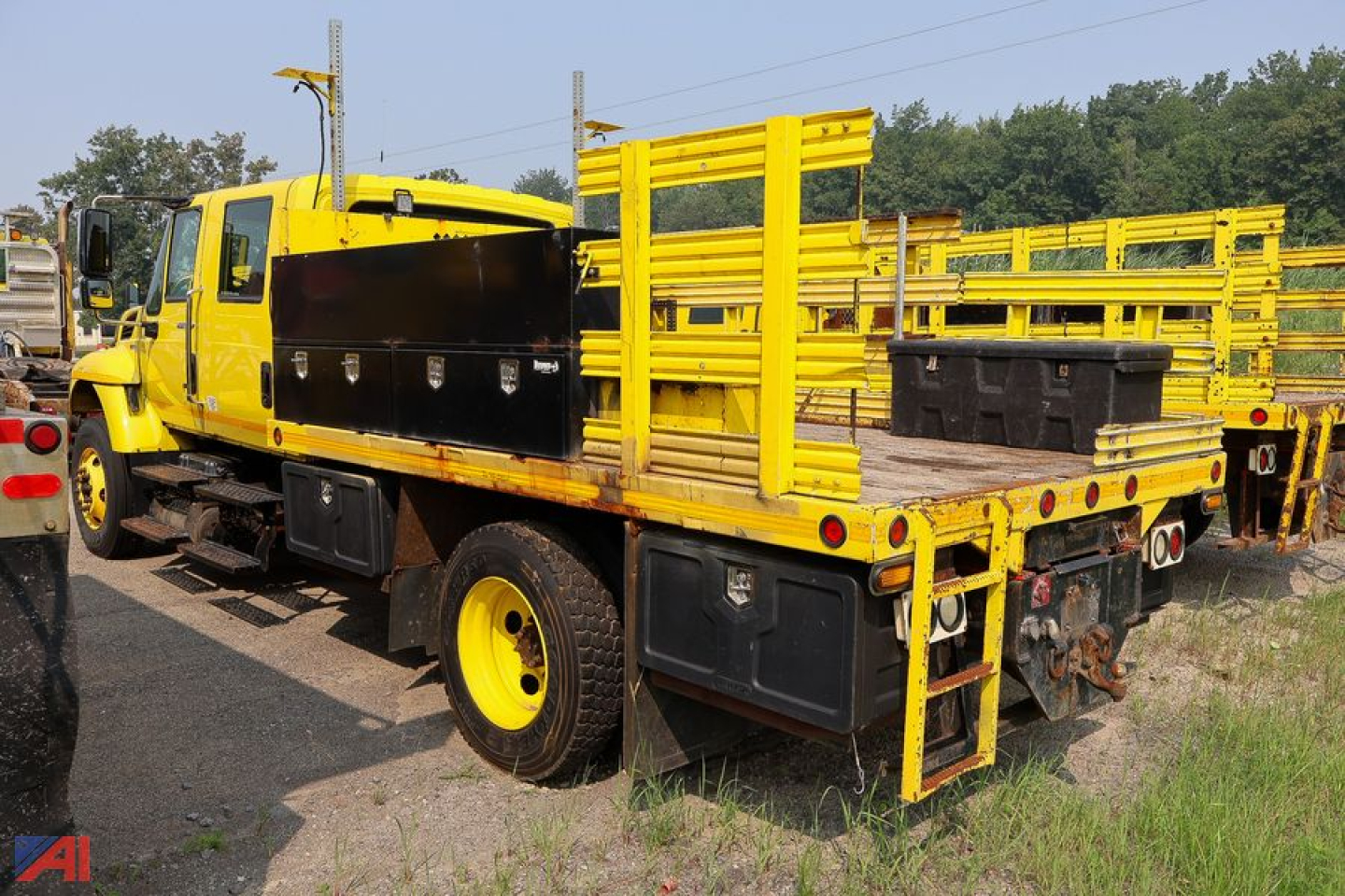 International WorkStar 7300 crew cab stake truck with yellow wooden stake bed and plow hitch, side toolbox, and heavy-duty rear rack.