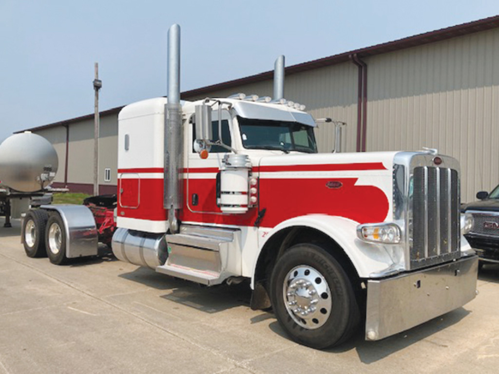 Peterbilt 389 extended hood truck in white and red with chrome exhaust stacks and large grille, industrial yard setting.