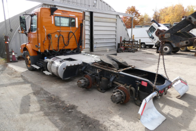 Orange Volvo VNM64T truck cab and chassis in a yard showing detached rear framing and mud flaps.