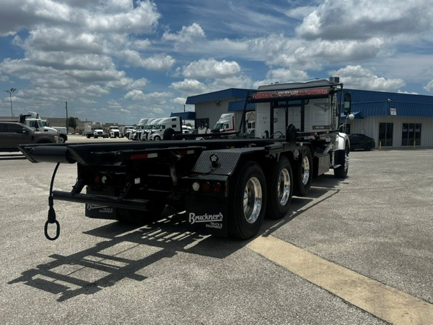 Side view of a 2020 Volvo VHD rolloff truck showing triple-axle rear, flatbed with hook, and taillights.