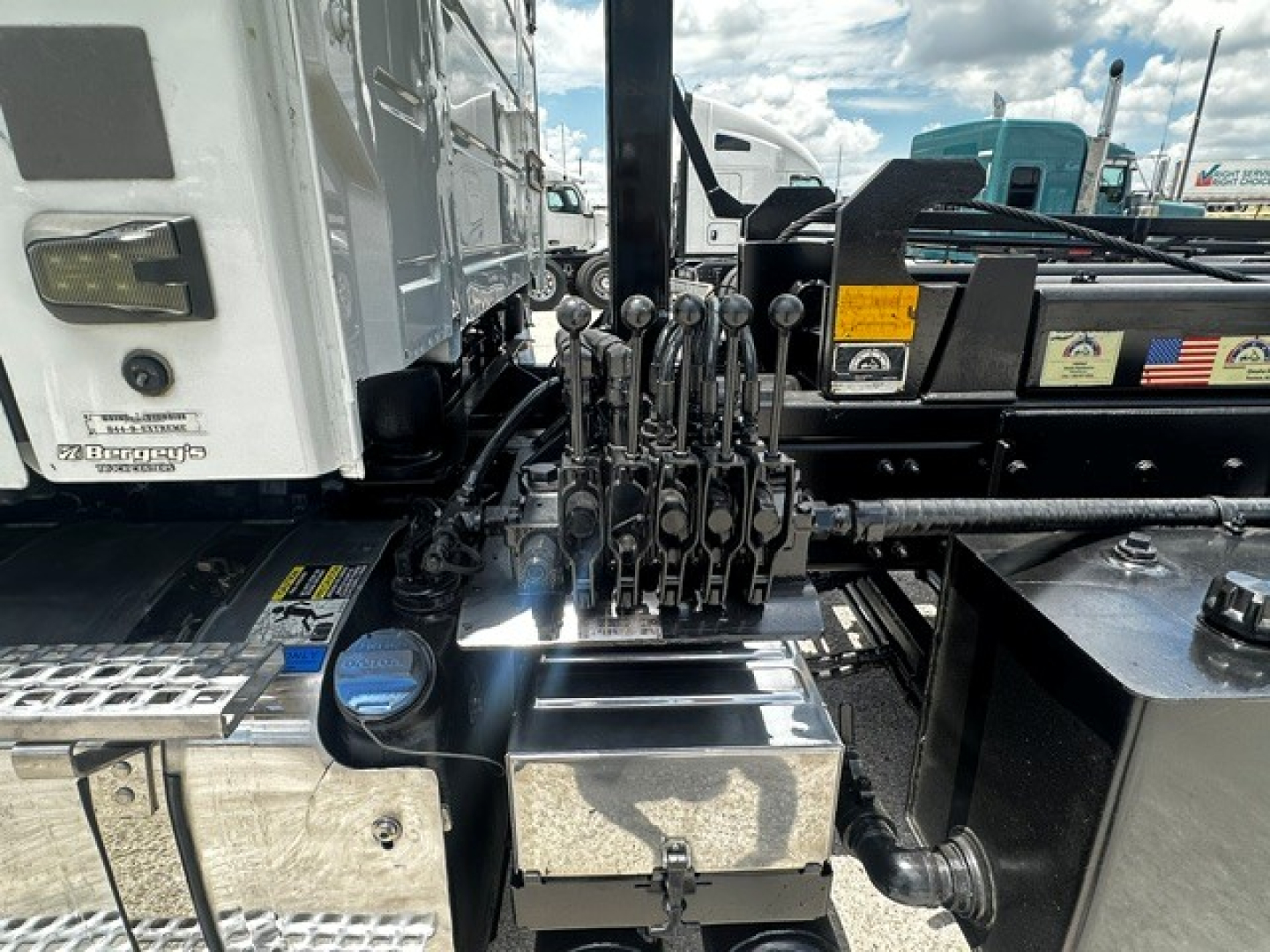 Rolloff truck cab area showing multiple control levers and chrome toolbox with metal steps in view.