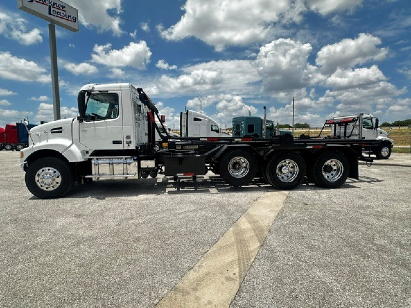 Volvo VHD truck in a lot showing a roll-off configuration with multiple axles and a white cab.