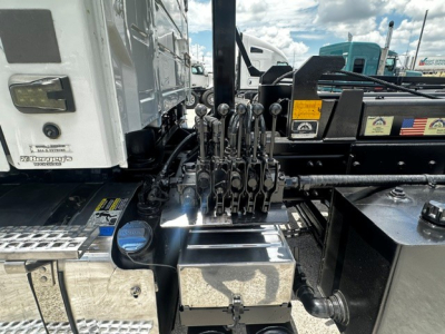 Rolloff truck cab area showing multiple control levers and chrome toolbox with metal steps in view.