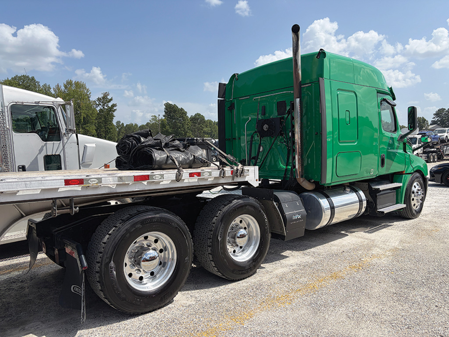 Truck cab and flatbed trailer showing green Freightliner Cascadia sleeper and chrome fuel tanks.