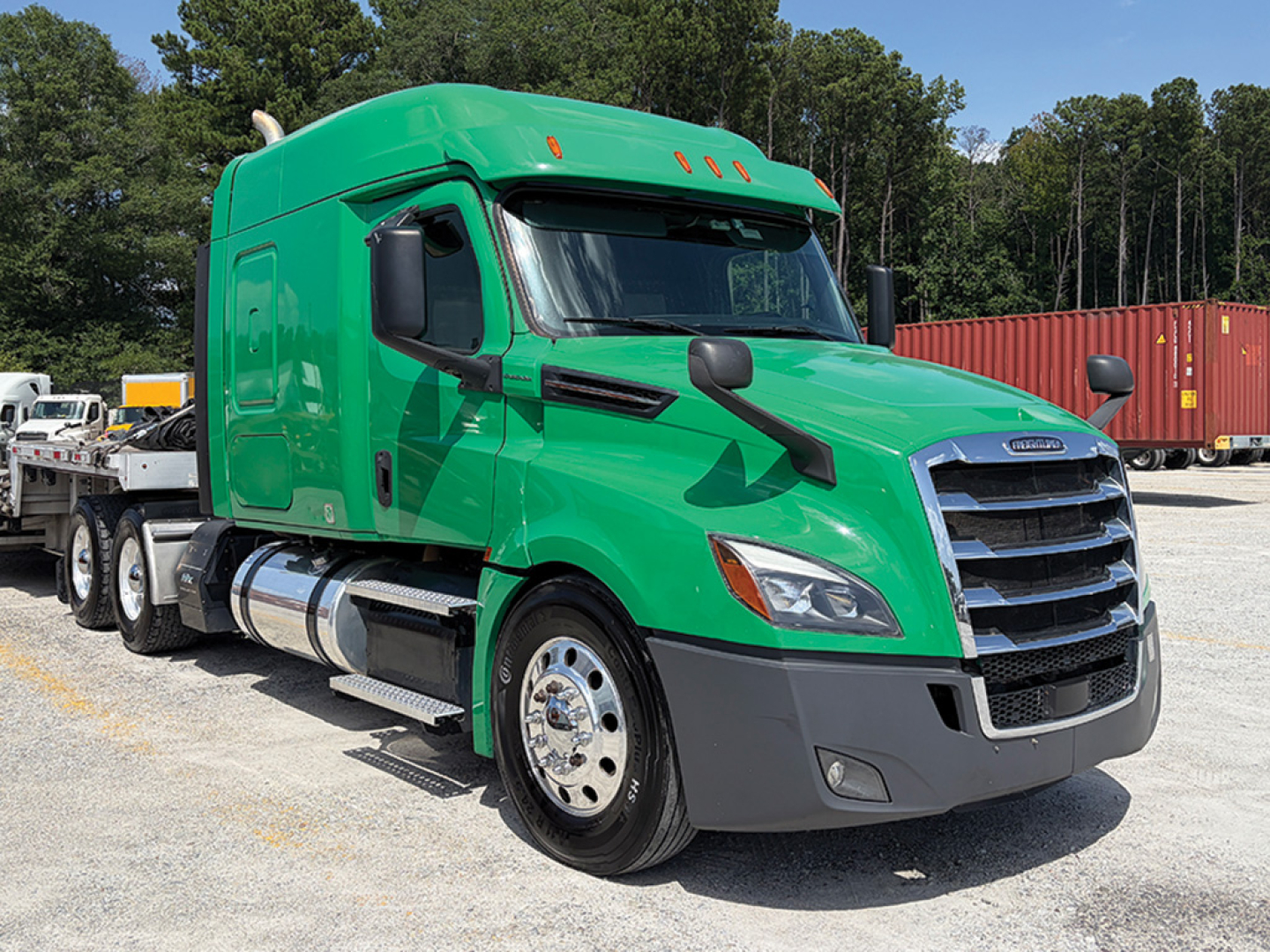 Truck cab and sleeper of a green Freightliner Cascadia 126 tractor from a front-right angle, showing chrome fuel tanks, black grille, and wheel area.