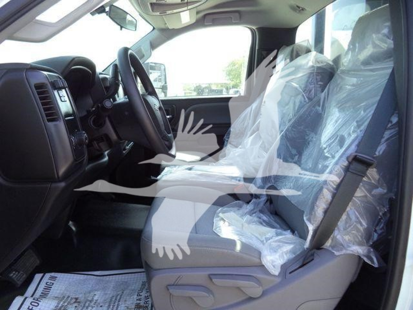 Interior of a new 2023 Chevrolet Silverado 6500HD roll-off truck showing plastic-wrapped front seats, steering wheel, and dashboard from the driver's side.
