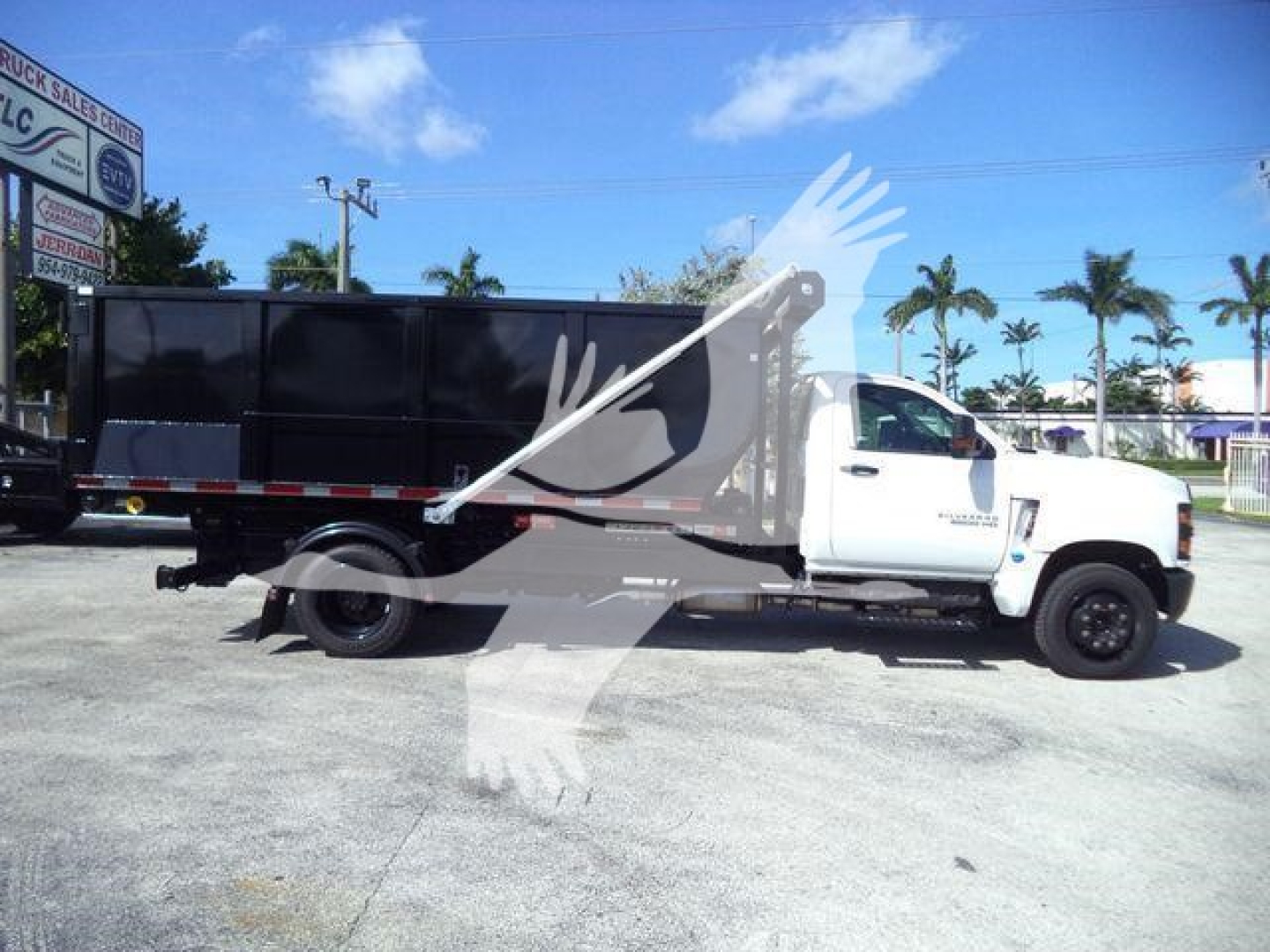 Truck: 2023 Chevrolet Silverado 6500HD roll-off body with black dump/box, white cab, side view showing longest wheelbase and dual rear wheels.