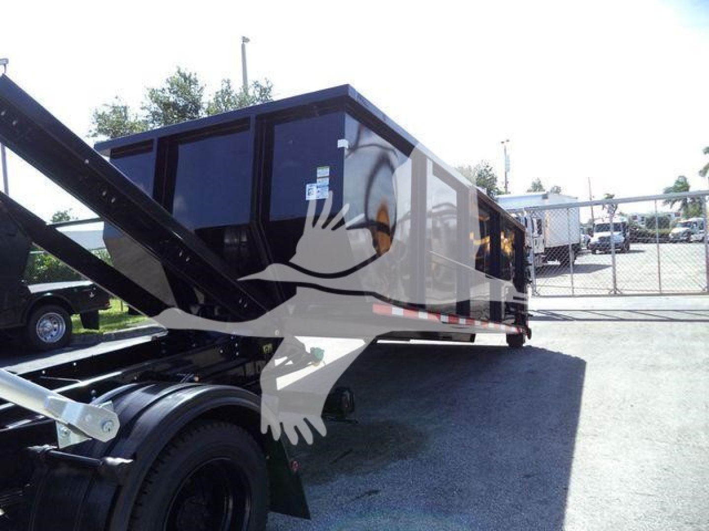 Vehicle body of a 2023 Chevrolet Silverado 6500HD rolloff truck with a large dark cabin and hydraulic arms visible, stock number J05565FM.