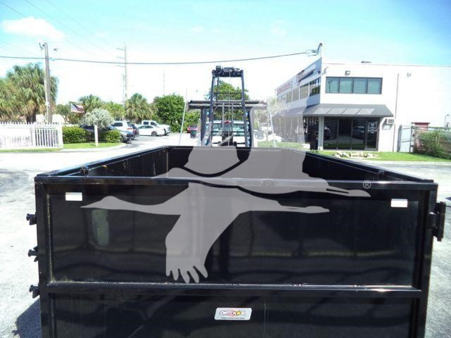 Truck bed of a 2023 Chevrolet Silverado 6500HD roll-off truck showing a black dump body with rear doors closed, parking lot in background.