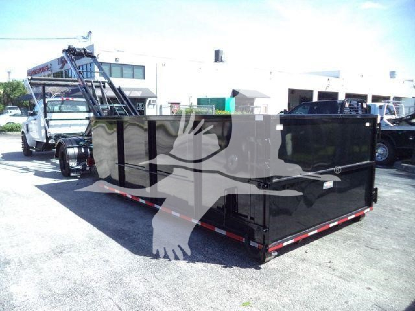 Chevrolet Silverado 6500HD roll-off truck with black dumpster body and hydraulic arm in a dealership lot, stock number J05565FM.