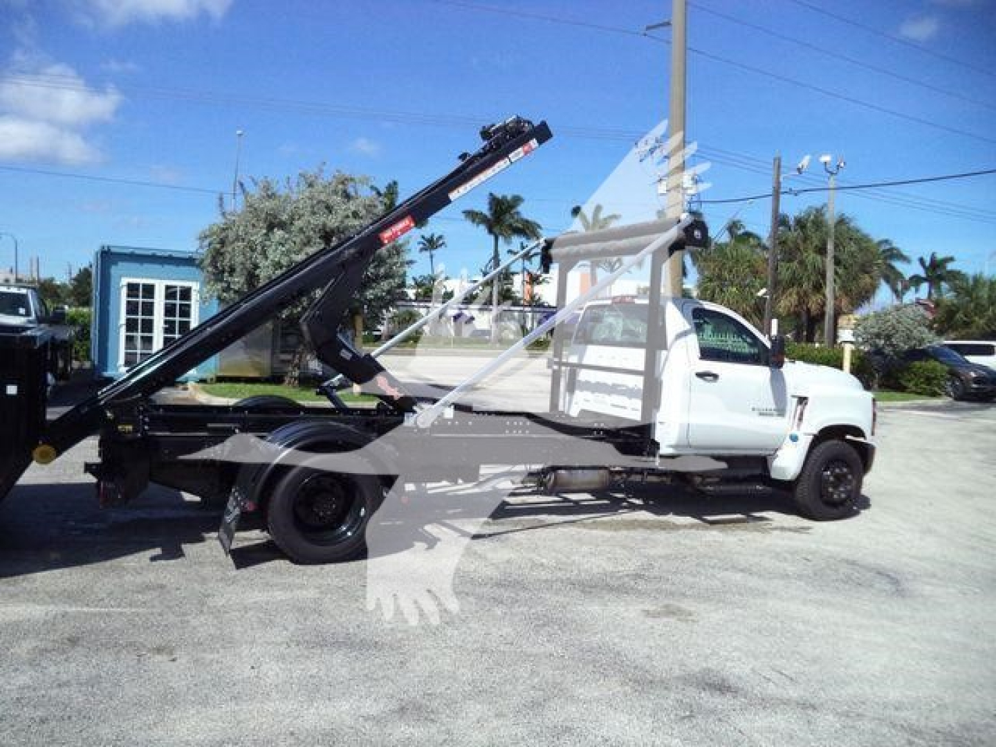 Flatbed tow truck with hydraulic boom on a white Chevrolet Silverado 6500HD, side view, in a dealership lot.