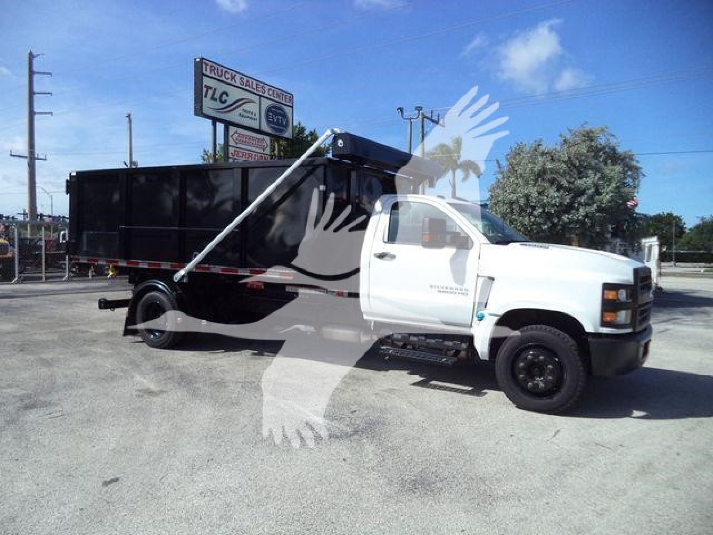 Truck bed with a black dump box on a white Chevy Silverado 6500HD cab and chassis, in a dealership lot.