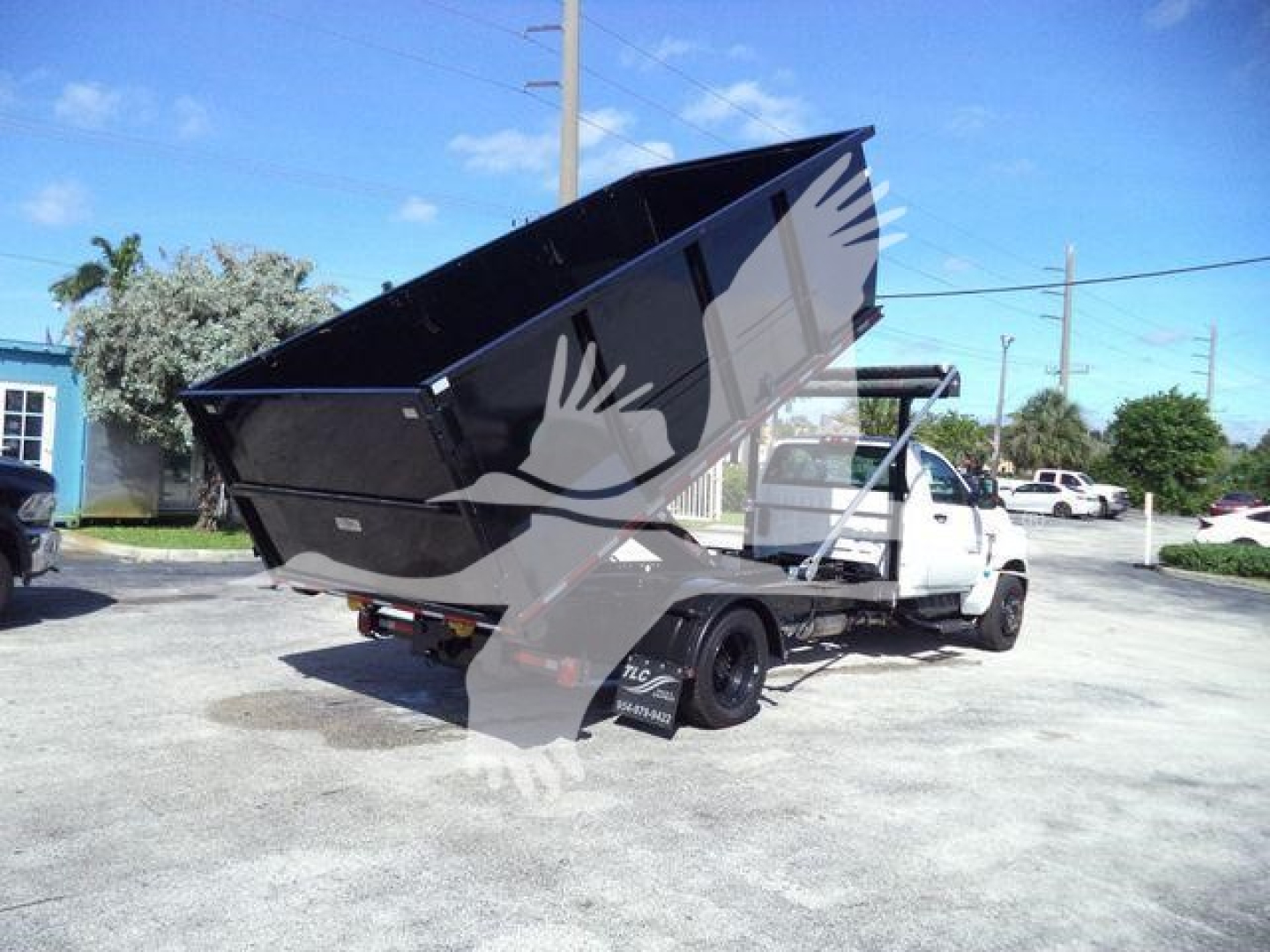 Dump bed truck in service position with hydraulic-hoist raised, Chevrolet Silverado 6500HD badge not visible, stock plate obscured. Clear sky, parking lot.