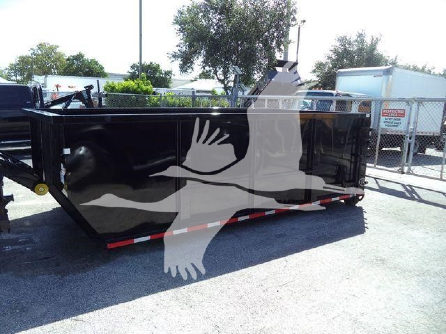 Truck bed with black dumpster-style container trailer in a lot, chevron reflectors along the rim, chain and latch at side, faint background signage.
