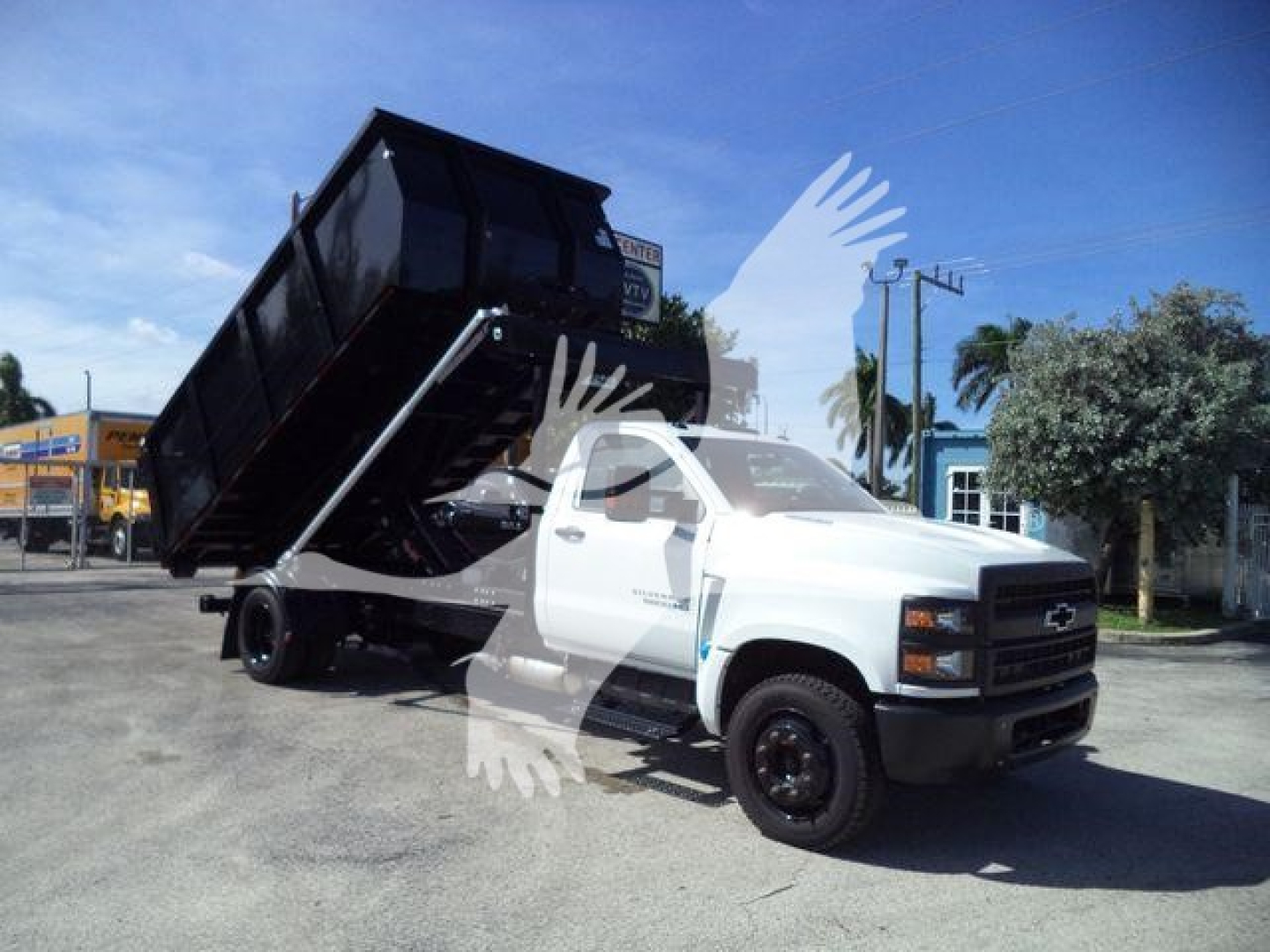 Chevrolet Silverado 6500HD dump truck in service lot, white cab, black dumping bed raised at angle. Stock number not legible in image.