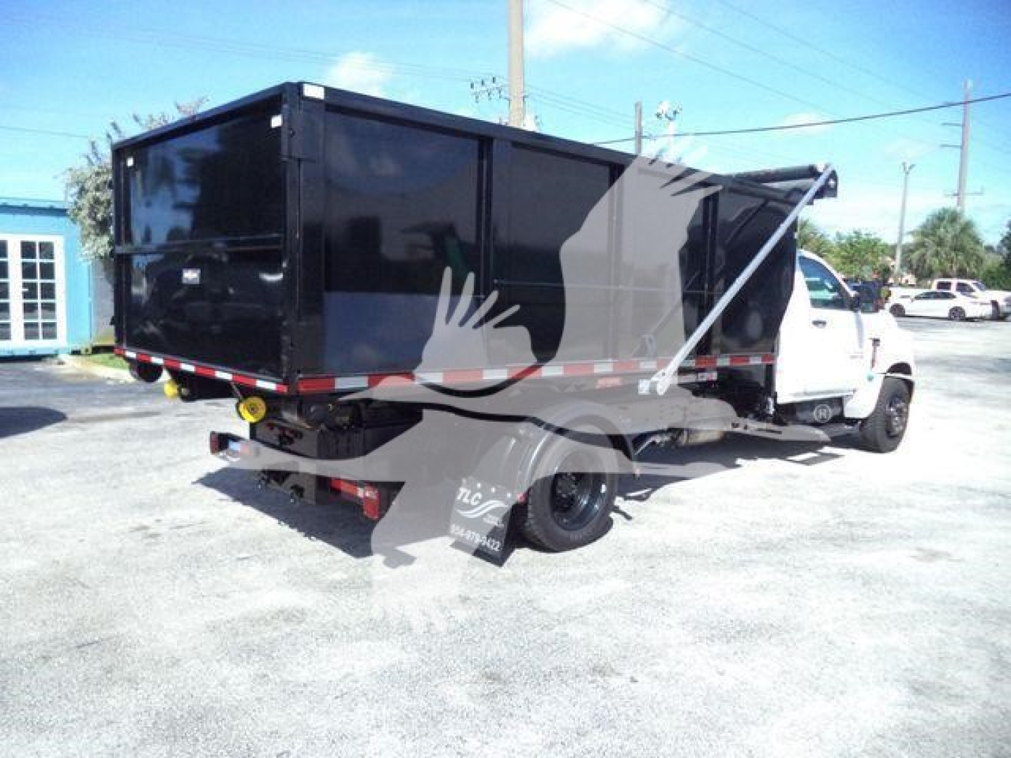 Truck with a black dump body on a white Chevrolet Silverado chassis visible from rear-right side; roll-off dumpster body with rear bumper and wheel wells.
