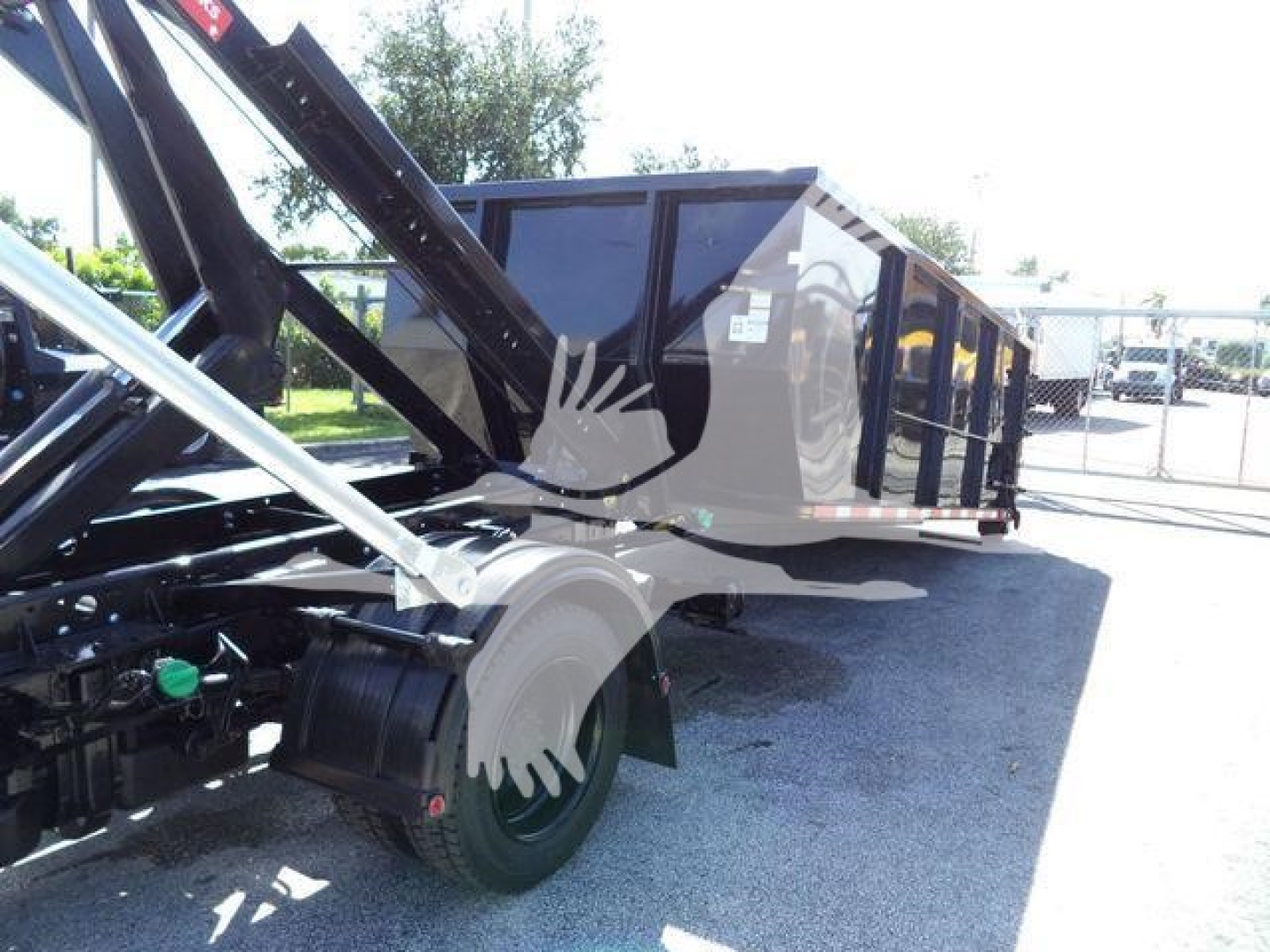 Truck bed area of a 2023 Chevrolet Silverado 6500HD roll-off, showing the hydraulic hoist framework and dump body, with chain mechanism and tires visible.