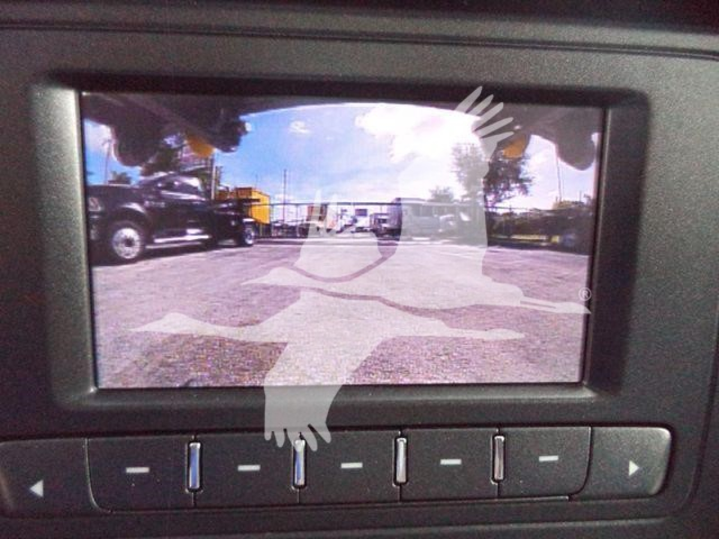 Truck interior screen showing rearview or camera display with reflection of outdoor lot and vehicles.