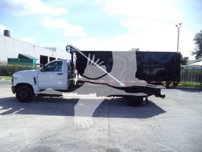 Truck side view: 2023 Chevrolet Silverado 6500HD roll-off body, white cab, black dump/box with graphic accents, stock number J05565FM.