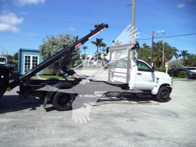 Flatbed tow truck with hydraulic boom on a white Chevrolet Silverado 6500HD, side view, in a dealership lot.