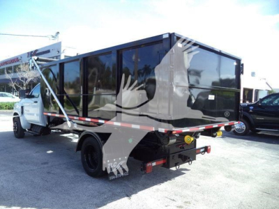 Truck-mounted refuse body on a white Chevrolet Silverado 6500HD chassis showing side of roll-off container with tinted panels and rear hookup.