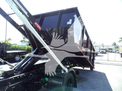 Truck bed dump/roll-off body on a Chevrolet Silverado 6500HD chassis showing hydraulic lift mechanism and dumping container, with stock number J05565FM visible.
