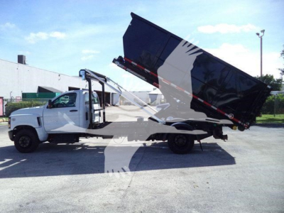 Truck side view of 2023 Chevrolet Silverado 6500HD rolloff showing cab and chassis with tilted dumping bed in raised position.