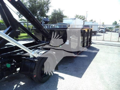 Truck chassis and equipment carrier with hydraulic arms in a dealership lot. side view shows trailer bed and tires.
