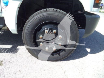 Truck front wheel showing heavy-duty wheel with black steel rim and lug nuts on a white Chevy Silverado 6500HD from a side angle.