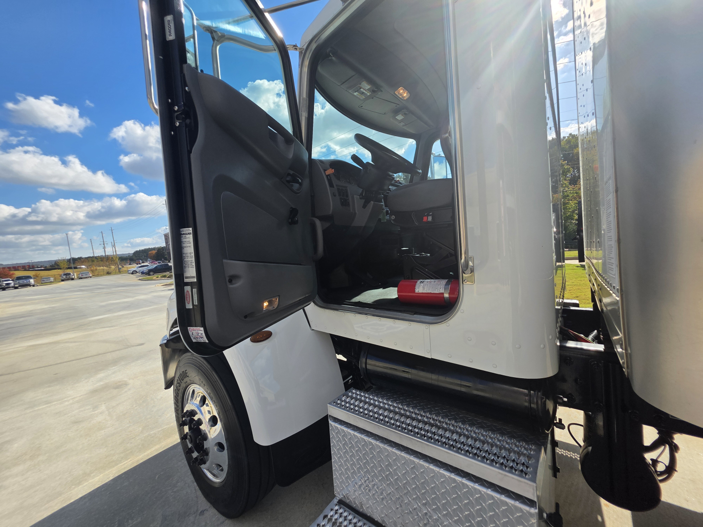 Peterbilt 337 cab entry with open door showing driver's seat, dashboard, and aluminum steps; front wheel and part of box truck cargo area visible.