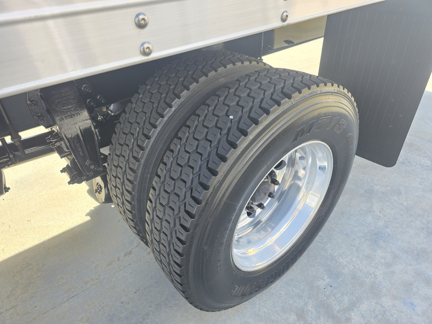 Peterbilt truck rear dual wheels showing tire treads and chrome rims. Partial underbody with black chassis and aluminum box side. No readable labels visible.