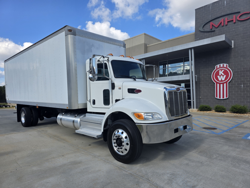 Peterbilt 337 box truck in front of dealership, side view showing cargo box and front grille.
