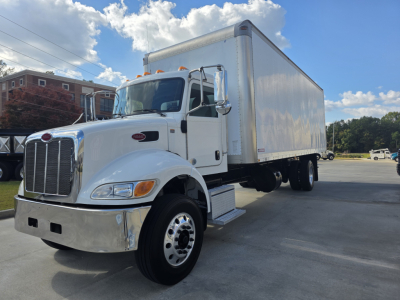 Peterbilt 337 box truck in a parking lot, white cab with chrome grille, large box cargo area; no visible warning labels readable on the image.