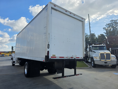 Peterbilt 337 box truck rear view showing large cargo box and rear underride guard, white exterior, chassis with wheels, parked in lot.