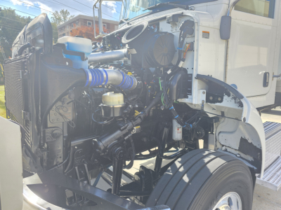 Peterbilt 337 engine bay showing radiator, air intake, hoses, and coolant reservoir in front of cab; visible engine components and wiring.