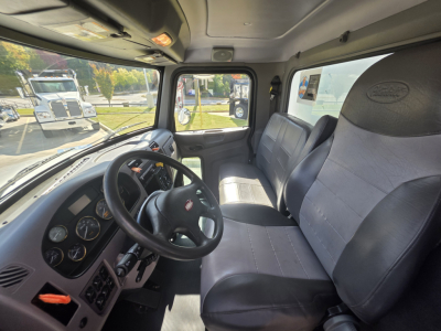 Peterbilt 337 interior cab view showing steering wheel, dashboard gauges, driver seat and passenger seat with grey vinyl. side window and view of other trucks outside.