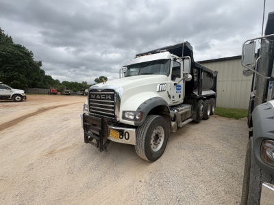 Mack GR84F dump truck in a gravel lot, front three-quarter view showing chrome grille, bumper with numbered sign, and dump bed.