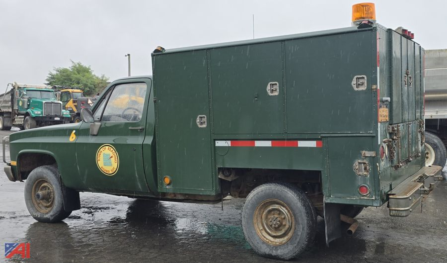 1986 Chevrolet D30 utility box pickup truck side view showing green cab with yellow emblem, large square utility box, amber beacon on cab roof, and mud-streaked tires.