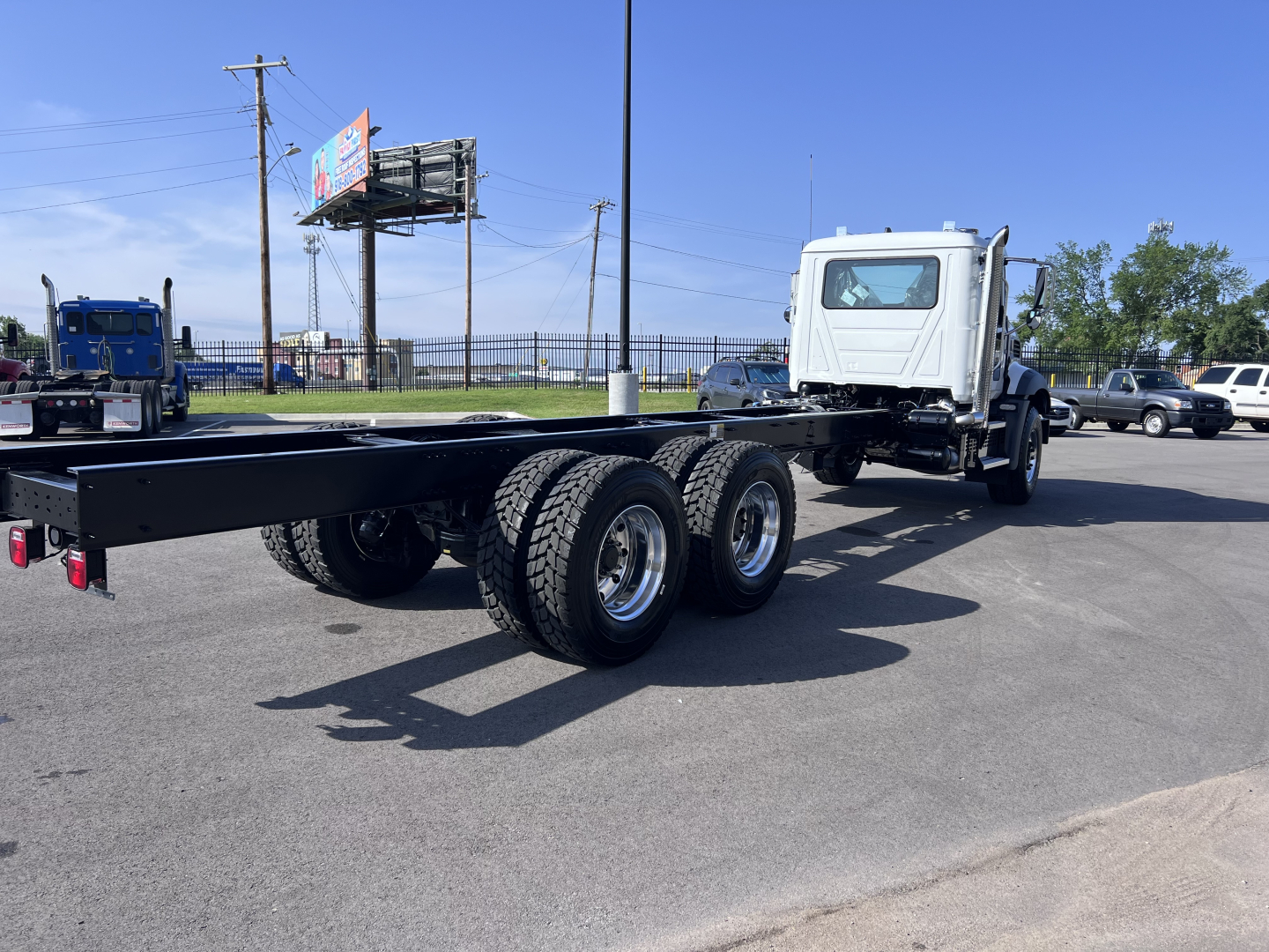 Chassis cab of a 2026 Mack GR64B truck showing a long unmounted frame with triple rear axles and a white cab in the background.
