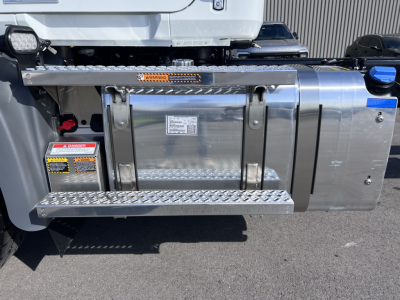 Truck fuel tank area on Mack GR64B cab and chassis showing polished metal fuel tank, step plates, safety labels, and hoses.