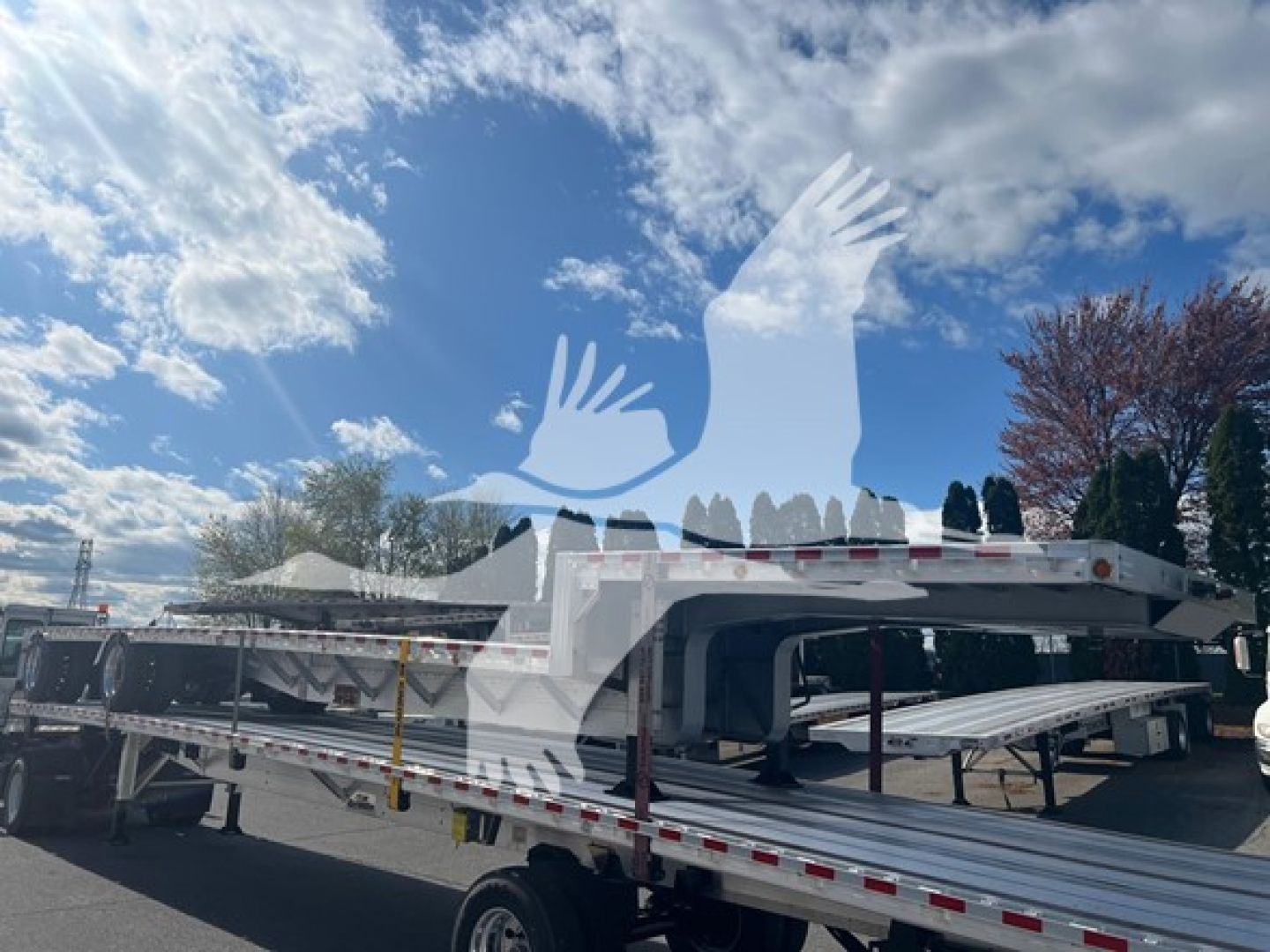 Drop deck trailer with flatbed sections and side rails, labeled Bubba Drop; white and silver with warning triangles and reflective tape.